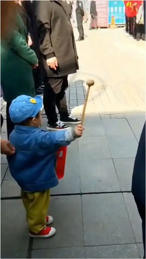  跟着街头方阵队敲锣打鼓男孩手拿按摩捶敲纸盒,看起来有模有样
